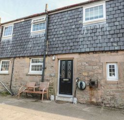 An outdoor view of a cottage with a bench and door at Shepherds Nook in Chathill