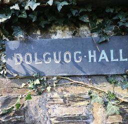 A sign reading Dolguog Hall attached to a stone wall with ivy at Plas Dolguog in Machynlleth