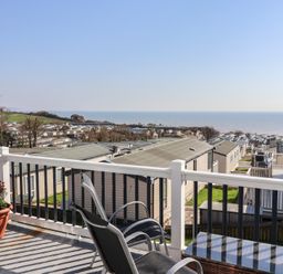 A balcony with a table and chair overlooking the sea at Bordeaux in Ladram Bay Otterton