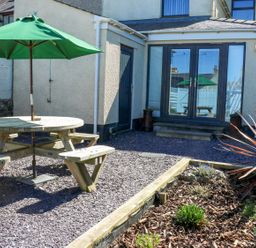 A garden with a table and benches under an umbrella at Rhiwlas in Rhosneigr