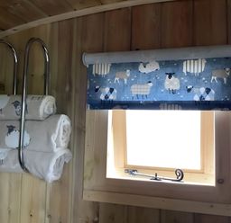 A bathroom with towels on a rack and a window with a roller blind at The Shepherds Hut at Hafoty Boeth in Corwen