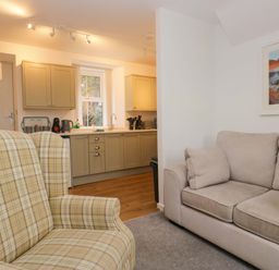 A living room with an armchair and a kitchen area at Bobtail Cottage in Kendal