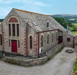 An exterior view of a building with a red door and windows at Kaber Chapel near Kirkby Stephen