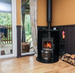 A living room with a wood stove and fire burning at Owls Nest Lodge South Molton