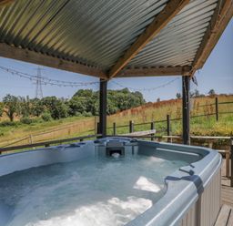 A hot tub under a canopy with a view of fields at Hedgehogs Lodge South Molton