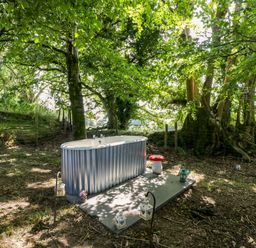 A bathtub placed on a concrete base in a forested outdoor area at Valley View Shepherd's Hut in South Molton