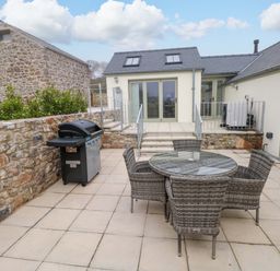 An outdoor area with a table and chairs beside a grill at Dairy Cottage in Oxwich