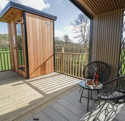 An outdoor seating area with a wooden shed and glass table at Dawn's Rest in Nantmel near Rhayader