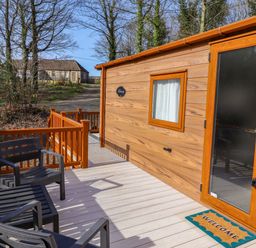A wooden cabin with a welcome mat and outdoor seating in front at Gardeners Lodge 