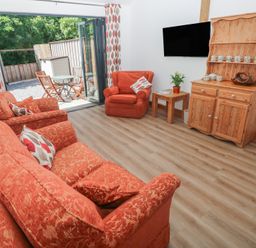 A living room with orange furniture and a television at Brookview Goldfinch in Haverfordwest