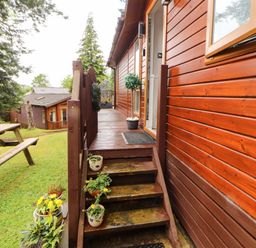 Steps leading to a wooden lodge with plants and a picnic table at Jodene Lodge, Redwood 2 Bowness-On-Windermere