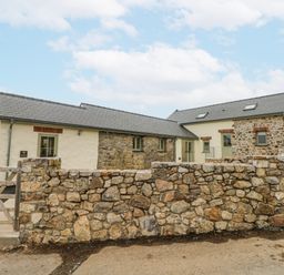 An outdoor view of a stone house and wall at Barley Cottage in Oxwich