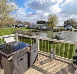 An outdoor seating area with a table and chairs overlooking a pond at 13 The Lakes in Mablethorpe