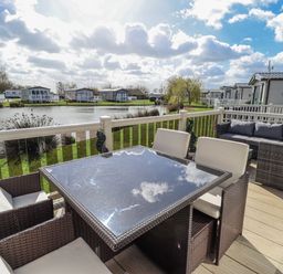 An outdoor area with a table and chairs near a lake at 13 The Lakes Mablethorpe