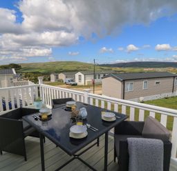 An outdoor patio with a table and chairs overlooking hills at Swanny View in Swanage
