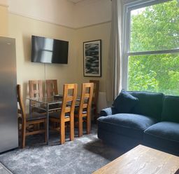 A living room with a dining table and chairs and a refrigerator at Apartment 5 in Torquay