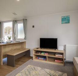A living room with a table and television at Shamrocks Cove Caravan