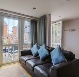 A living room with a sofa and sliding doors leading to outdoor seating at Beck House Weymouth