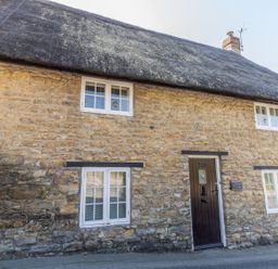 A stone cottage with a thatched roof and windows at Honeypot Cottage in Weymouth