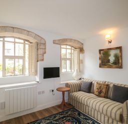 A living room with a sofa, table, and windows at Longfords Mill near Nailsworth