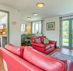 A living room with a red sofa and dining area at Wren Cottage in Cowbridge
