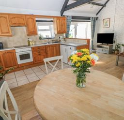 A kitchen with wooden cabinets and a dining table with flowers at Daffodil Cottage in Blaencwm near Treorchy
