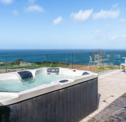 An outdoor space with a hot tub and chairs overlooking the ocean at tbc in St. Ives