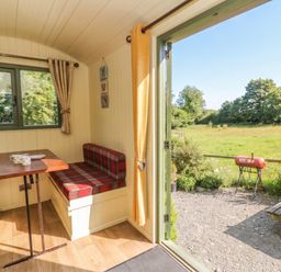 A dining area with a table and benches overlooking a garden at The Three Spaniels Shepherds Hut in Cwrtnewydd near Llanybydder