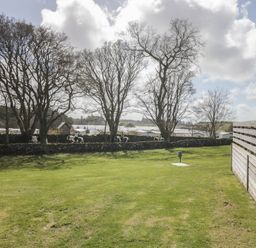 A garden with trees and a stone wall at Standard Caravan at Three Lochs Holiday Park, Newton Stewart