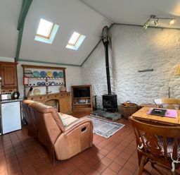 A living room with a sofa, table, and stove at Starling Cottage near Cowbridge