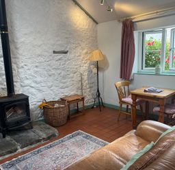 A living room with a stove, basket, and table at Starling Cottage near Cowbridge