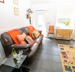 A living room with a brown leather sofa with cushions and a red throw a glass table with a wine bottle and two glasses a wooden chair a foldable wooden table a wall-mounted television and a patterned rug at Bridge Cottage in Haltwhistle near Hadrian's Wall