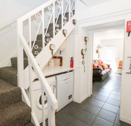 A staircase with carpet and a laundry area with washing machine and dishwasher underneath the stairs leading into a living room with a sofa at Bridge Cottage in Haltwhistle near Hadrians Wall