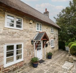 A stone cottage with a thatched roof and pathway at Woodbine Cottage in Weymouth