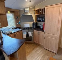 A kitchen with appliances and wooden cabinetry at 2-Bed Caravan, Sleeps 6 w/ Parking, No Pass Needed