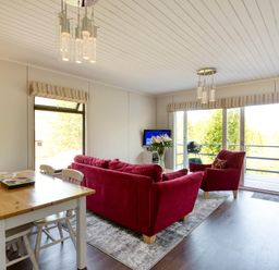 A living room with a sofa, armchair, dining table and television at 2 bedroom lodge with stunning loch, mountain views Crianlarich