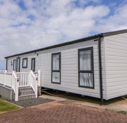 A mobile home with a deck next to a paved area at The Dorchester at Bay View New Quay