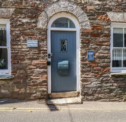 A stone wall with a blue door and windows at Stones Throw in Mevagissey