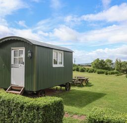 A shepherd's hut with a door and windows on a grassy area at Shepherds Hut at East Hill Pride Four Elms Hill Nr. Sidmouth