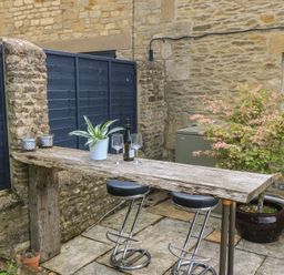 An outdoor seating area with a wooden table and bar stools at 2 The Gardens Lechlade