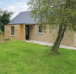 An outdoor view of a house with a door and windows at Mayfly Cottage