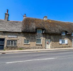 A thatched cottage with stone walls and front door at Little Wickers in Corfe Castle