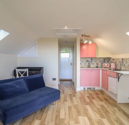 A kitchen area with a sofa and pink cabinets at Hay Loft at Ebenezer Chapel in Milwr