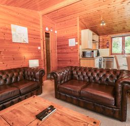A living room with brown sofas and a kitchenette at 89 Ambleside in White Cross Bay