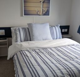 A bedroom with a bed and wall art at Presthaven - Denbigh Dunes Gronant