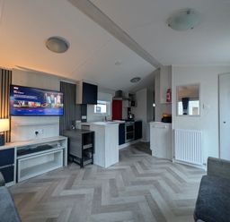 A living room with a tv and kitchen area at Presthaven - Denbigh Dunes in Gronant