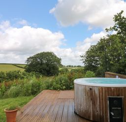 An outdoor space with a hot tub and wooden deck at Reddaway Byre Okehampton