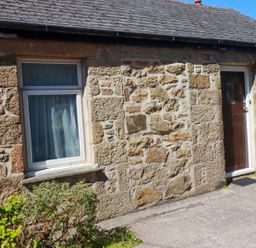 An exterior view of a cottage with a stone wall and window at Chyancrowse in Penzance