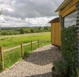 A view of a gravel path leading to a metal and wooden shed with flower pots at The Little Shepherds Hut with a View Builth Wells
