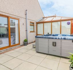 A patio area with a hot tub and sliding doors at Smithy Cottage in Cemaes Bay